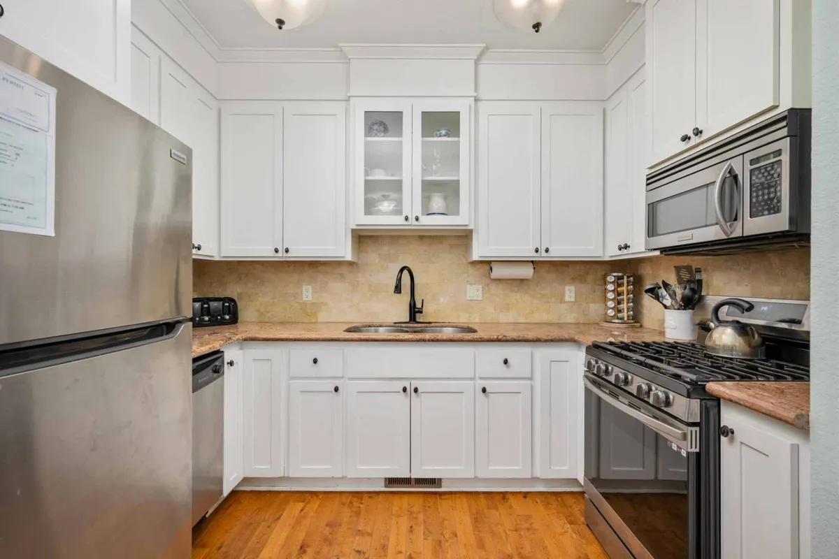 A gourmet kitchen boasting stainless steel appliances, granite countertops, pristine white cabinetry, and a prominent kitchen sink. The space is designed for cooking, gathering, and entertaining, with ample room for shared meal-prep and conversation.