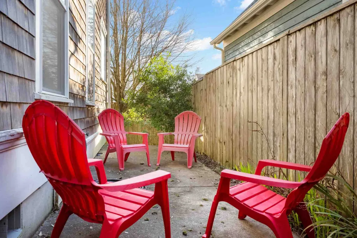 Four vibrant red Adirondack chairs are arranged for conversation and relaxation against a backdrop of green foliage and a wooden fence. The sunny, open yard invites both play and leisurely chats.