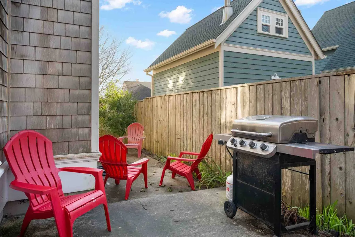 Bright red chairs are arranged next to a grill in a cheerful, fenced backyard space, evoking a sense of casual outdoor fun. The setting suggests opportunities for barbecuing, socializing, and spending time together in the fresh air.