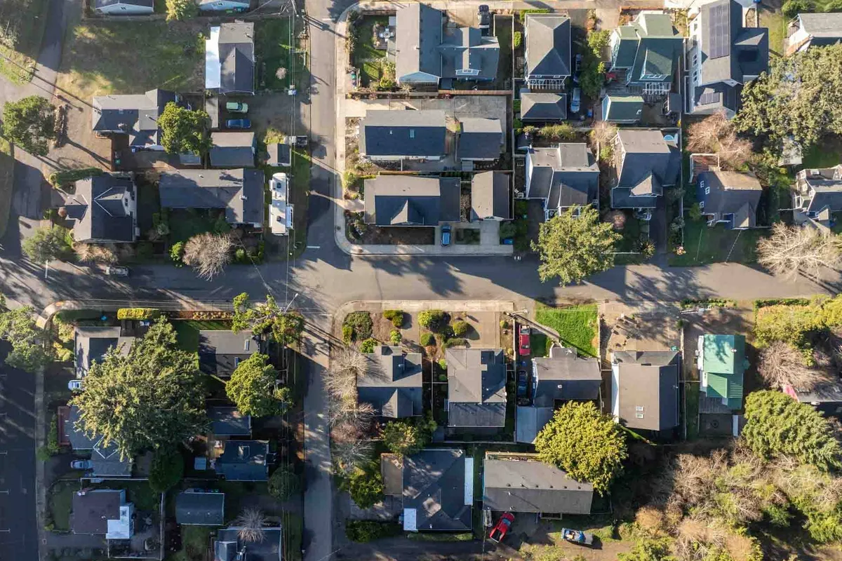 A peaceful neighborhood scene featuring residential homes surrounded by leafy tree canopies, with well-maintained sidewalks inviting families to walk, bike, and play outdoors. The view encompasses several homes and the overall friendly, welcoming atmosphere of the area.