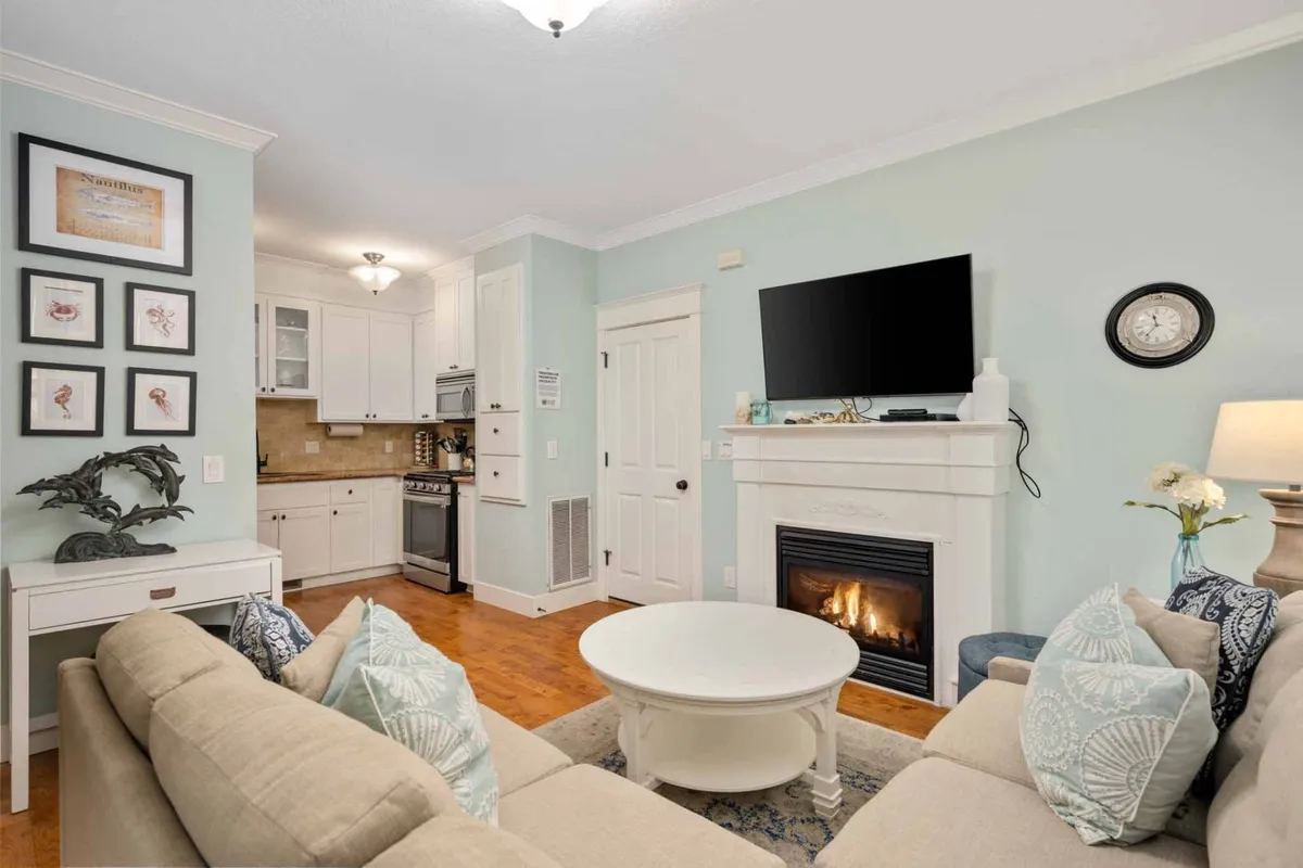 The image shows a cozy living room with a roaring fireplace as the focal point, surrounded by a plush sofa, a stylish coffee table perfect for games or snacks, and whimsical wall art that adds a playful, storybook charm. The warm ambiance invites guests to relax, socialize, and make memories together.