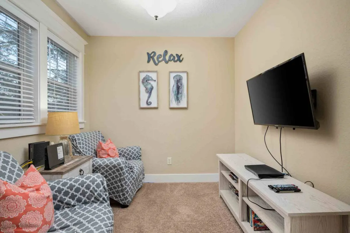 A comfortable, softly-lit space with armchairs, a television, decorative wall art, and a lamp, arranged in a way that invites relaxation and group activities. The furniture layout supports both solo downtime and shared entertainment.