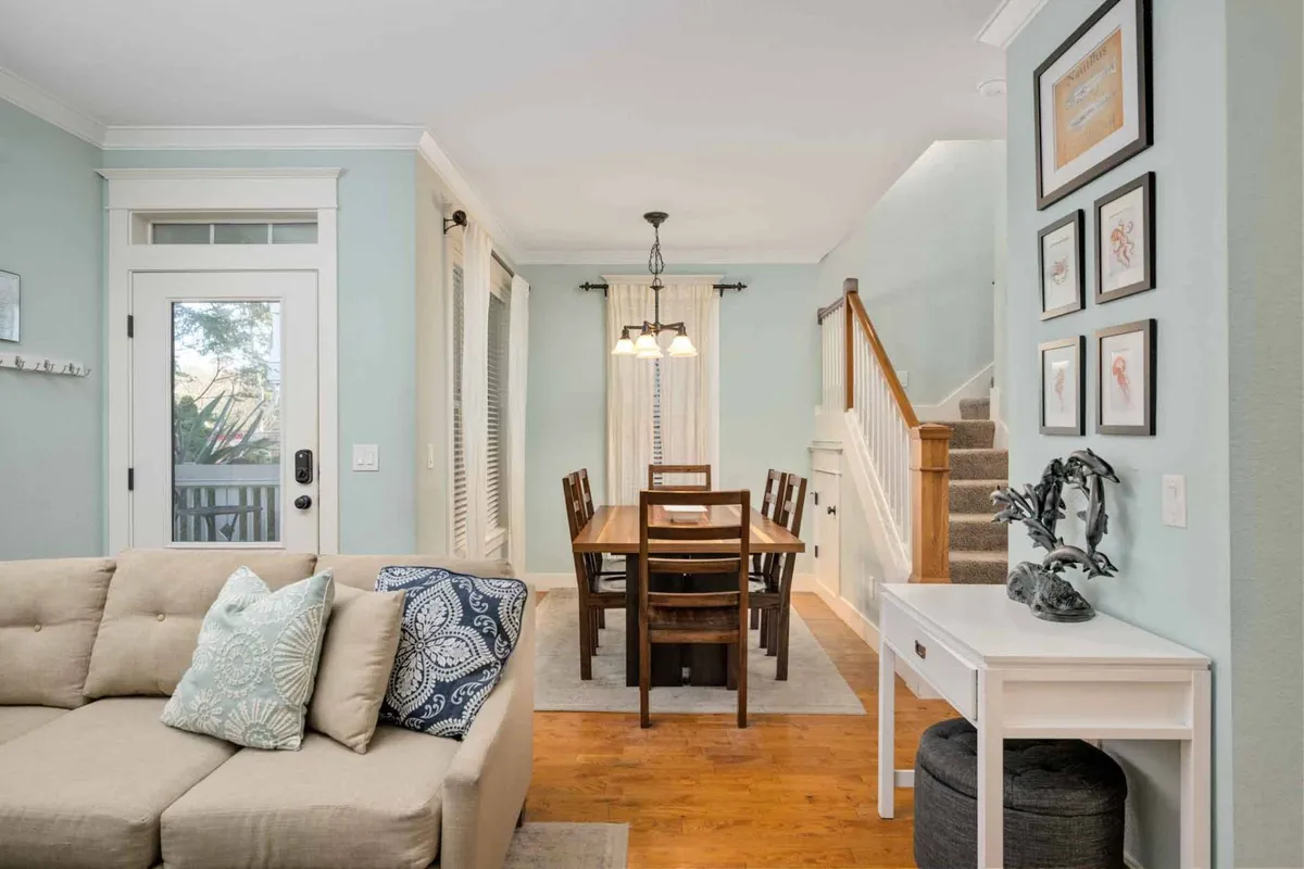An open-plan space featuring a comfortable sofa, a dining table set for meals, a graceful staircase, and whimsical wall art. The arrangement encourages easy flow between relaxing and dining, while decorative touches enhance the storybook charm.