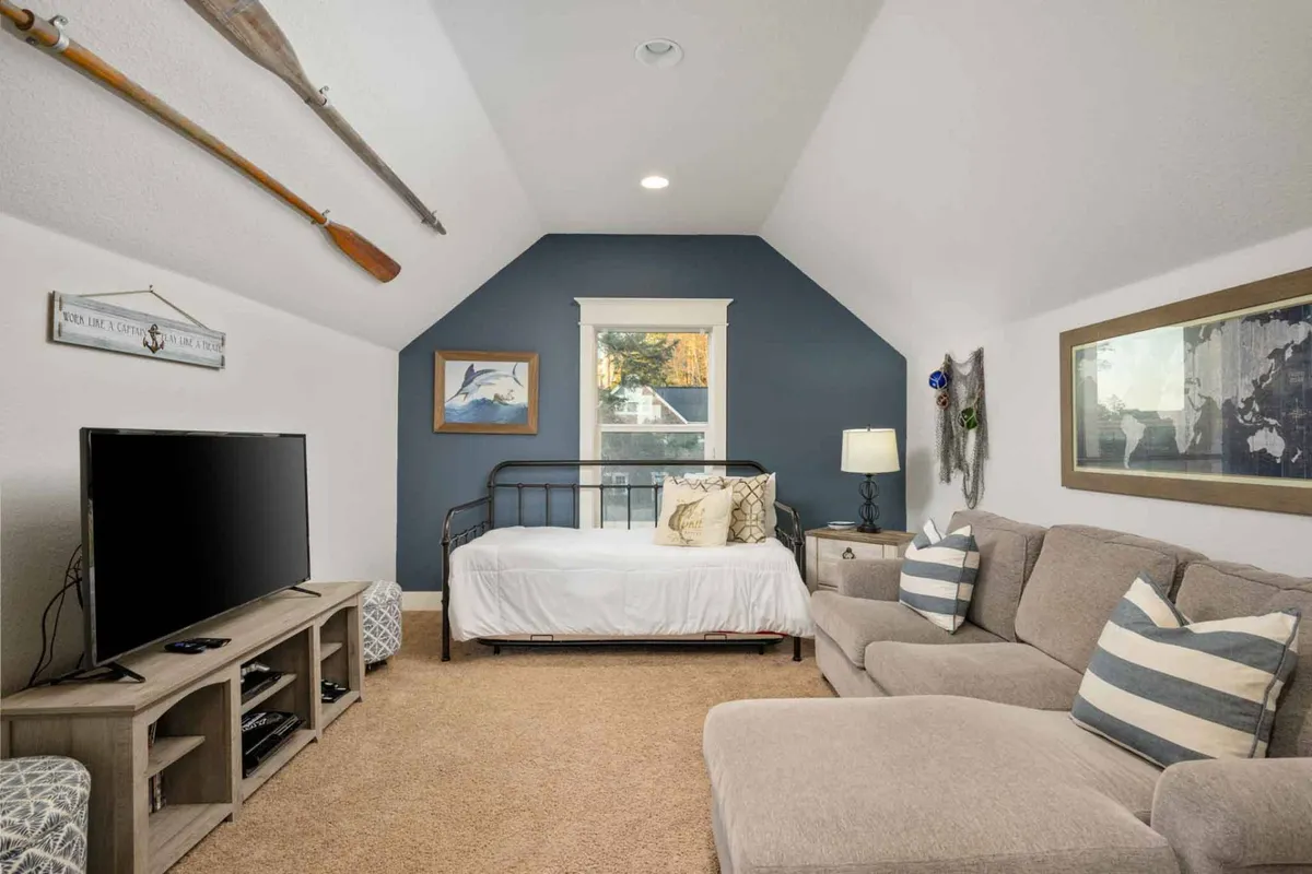 A welcoming bonus room with a bed, sofa, television, wall art, and a window. The space is comfortable and versatile—ideal for movie nights or quiet reading, as described for the third-floor bonus room.