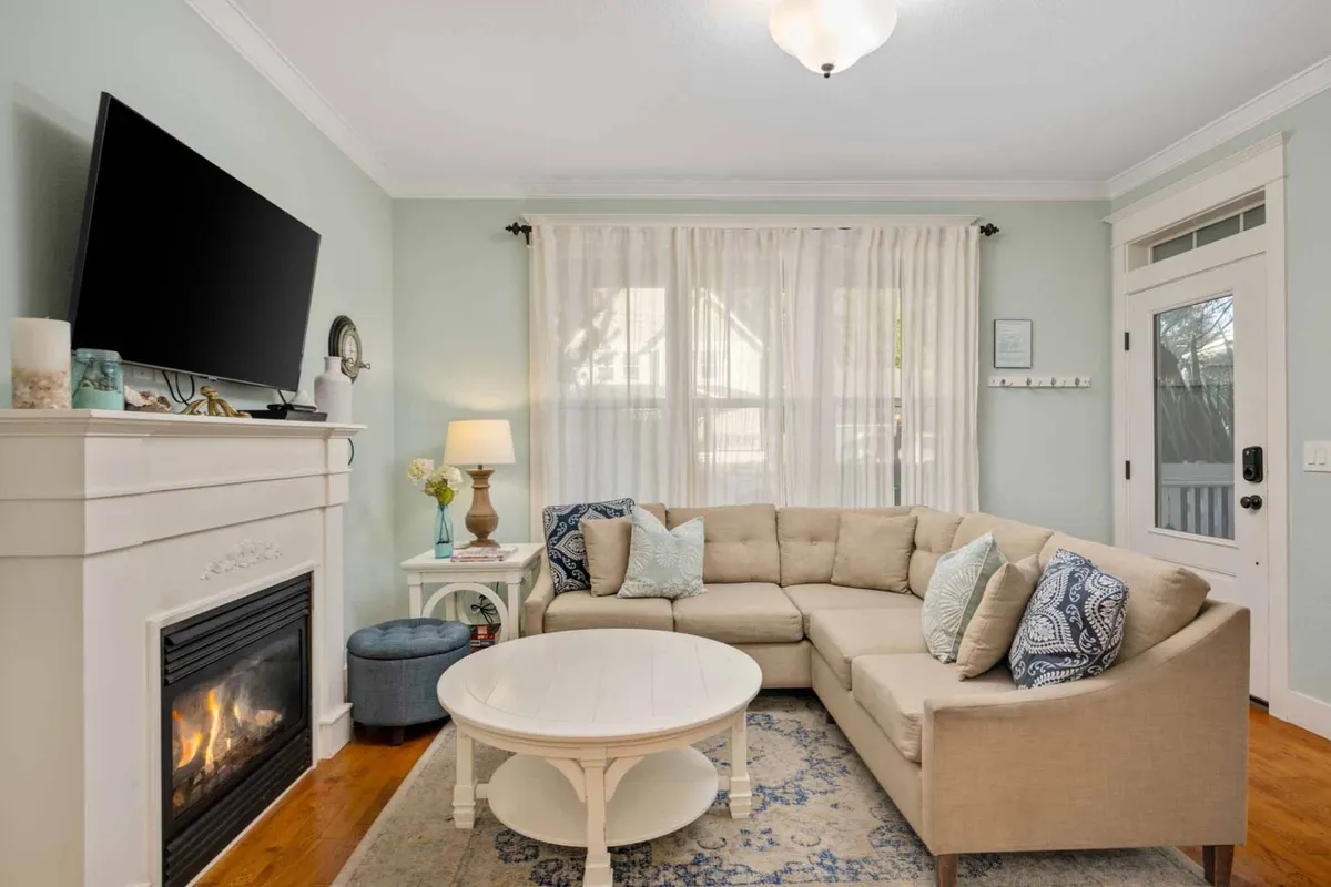 A cozy living area with a sectional sofa arranged around a coffee table, a warm gas fireplace, and a large television. Soft lighting and a lamp add to the inviting ambiance, creating the perfect space for relaxation and movie nights.