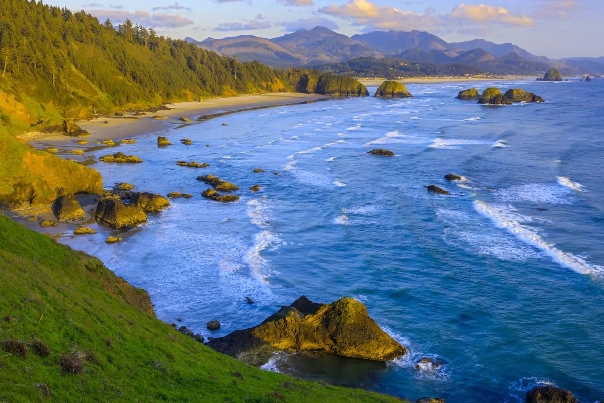 A tranquil view of the rocky coastline, gentle waves, sandy beach, and distant mountains. The expansive landscape invites beachcombing, picnicking, and exploration—activities perfect for families seeking adventure beyond the cottage.