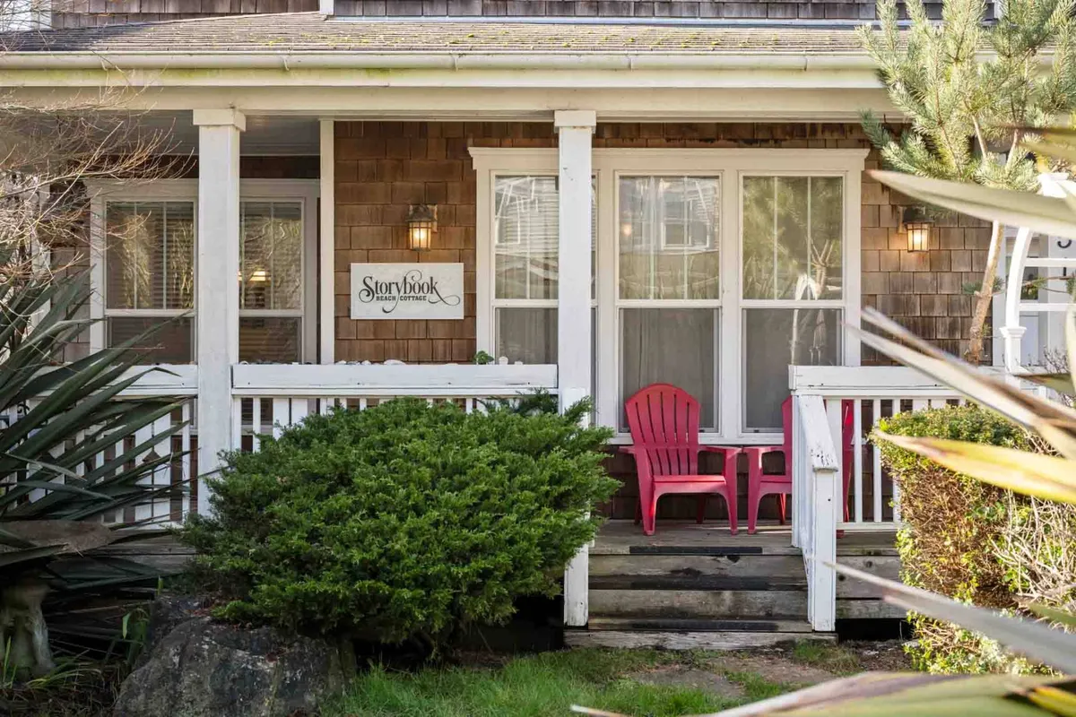 A welcoming front porch with pink chairs, the 'Storybook' sign, and lush greenery framing the entrance. The porch is set up for relaxation, with spots to enjoy coffee, read a book, or gather with friends.